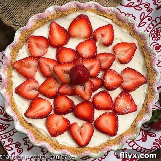 A vibrant overhead view of a whole Strawberry Cheesecake Ice Cream Pie, showcasing the glossy, ruby-red strawberry topping and the creamy white ice cream filling within a golden graham cracker crust