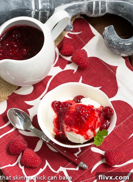 Overhead view of a Cheesecake Ice Cream Sundae generously topped with fresh raspberries and a pitcher of raspberry sauce on the side