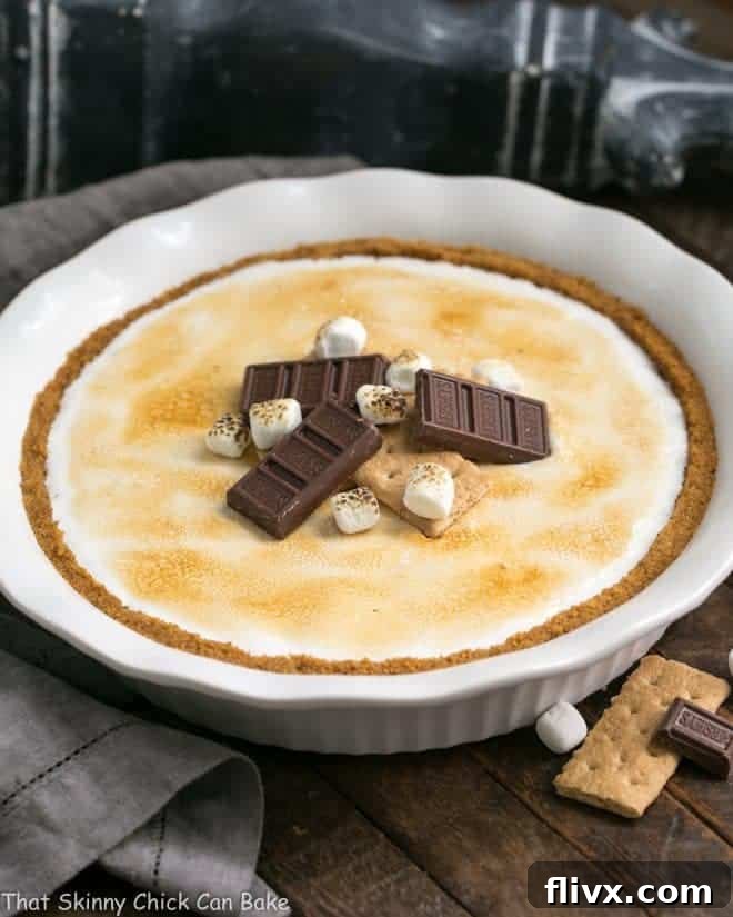 A stunning S'mores Pie in a white pie plate, adorned with extra chocolate pieces and miniature marshmallows for garnish