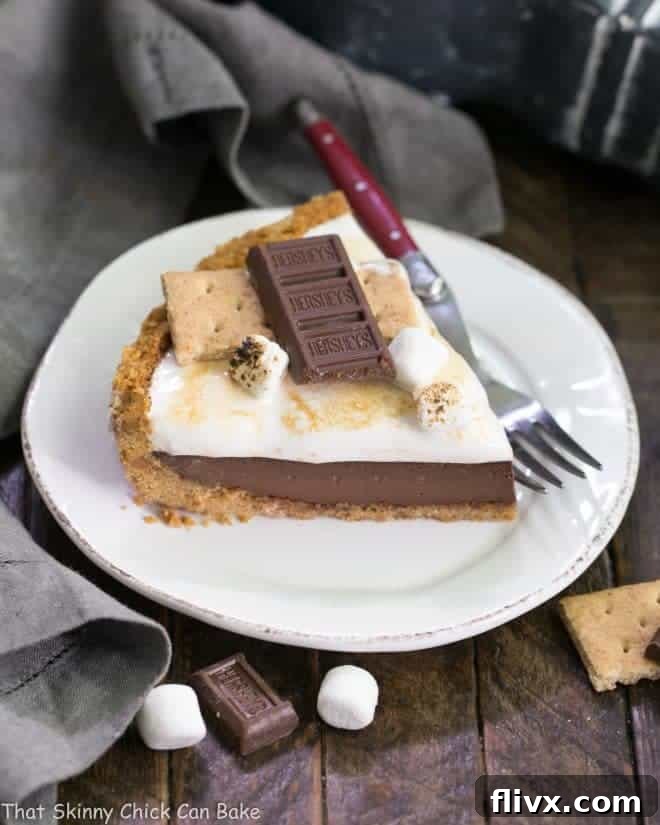 A close-up of a S'mores Pie slice on a dessert plate, with a red-handled fork ready for indulgence