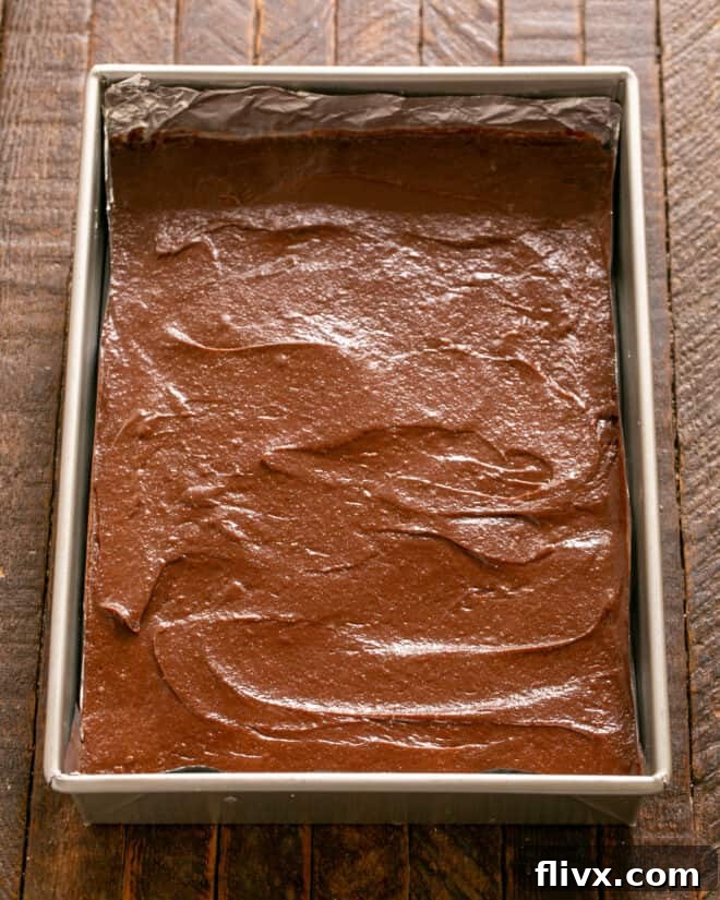 Rich brownie batter spread evenly over the shortbread crust in the baking pan.