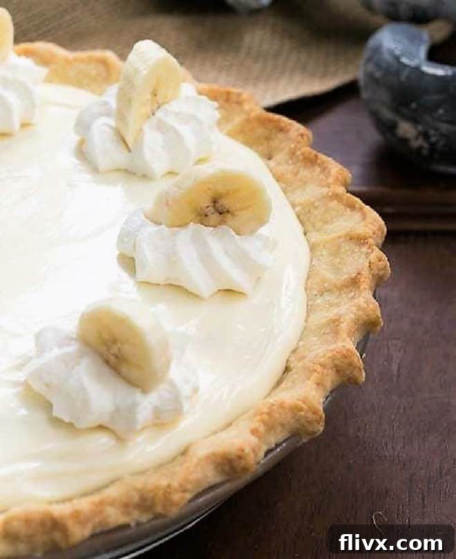 Close-up view of a slice of Banana Cream Cheesecake Pie, showcasing its layers of creamy filling, fresh bananas, and a generous swirl of whipped cream on top, garnished with a banana slice.