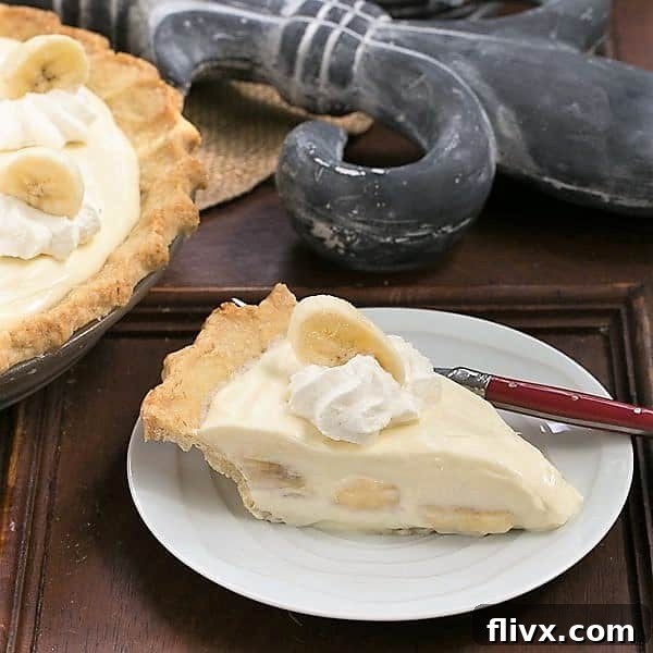 A perfectly portioned slice of Banana Cream Cheesecake Pie sitting on a elegant white dessert plate, showing off its beautiful layers and creamy texture.