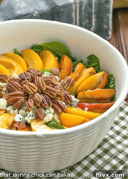 Close-up shot of a white textured serving bowl filled with Spinach Salad featuring perfectly grilled peach slices, crunchy toasted pecans, and generous crumbles of blue cheese, all elegantly arranged and lightly drizzled with dressing.