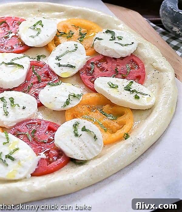 Pizza Margherita ready for the oven, topped with fresh slices of mozzarella, tomatoes, and basil.