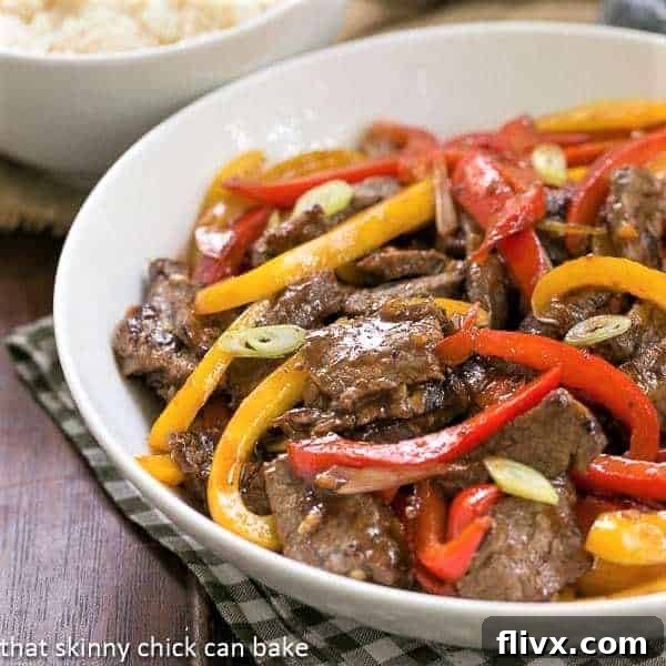 Asian Beef with Peppers in a white serving bowl, garnished with fresh scallions.