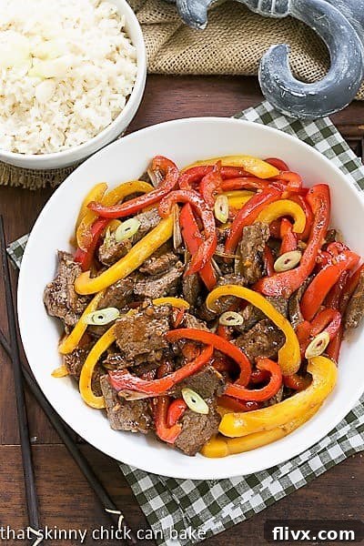 Overhead view of Asian Stir Fry Beef with vibrant peppers and scallions in a white bowl over a checkered napkin, highlighting its freshness and appeal.