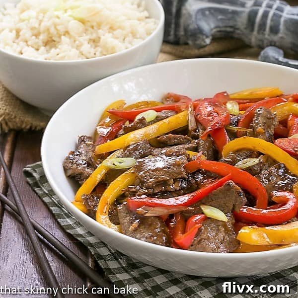Asian Beef with Peppers in a white serving bowl with a side dish of fluffy white rice, ready to be enjoyed.