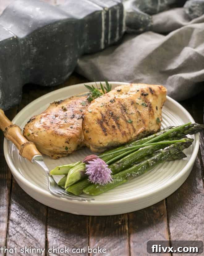 Two exquisitely grilled chicken breasts elegantly presented on a dinner plate, accompanied by tender asparagus spears and a bamboo-handled fork, awaiting enjoyment.