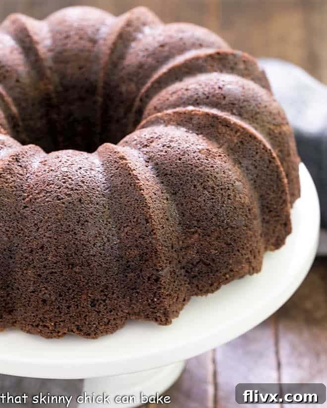 A beautifully baked Chocolate Zucchini Bundt Cake resting on an elegant white cake plate, ready to be sliced and enjoyed.