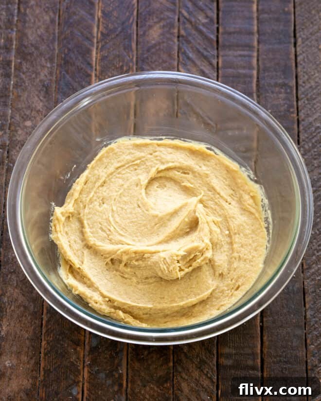Hands cracking eggs into a bowl with creamed butter and sugar, preparing to mix.
