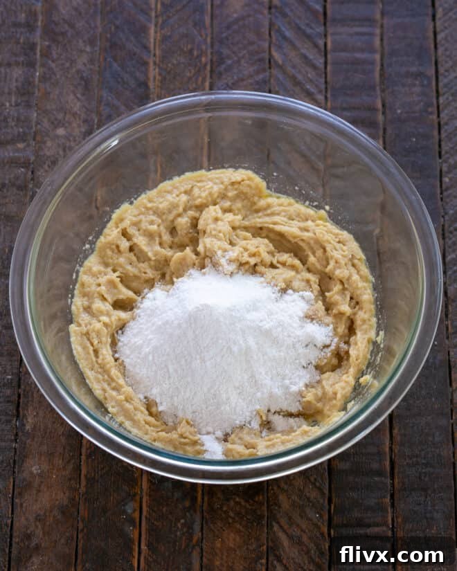 Instant vanilla pudding mix being added to a cookie dough mixture in a bowl.