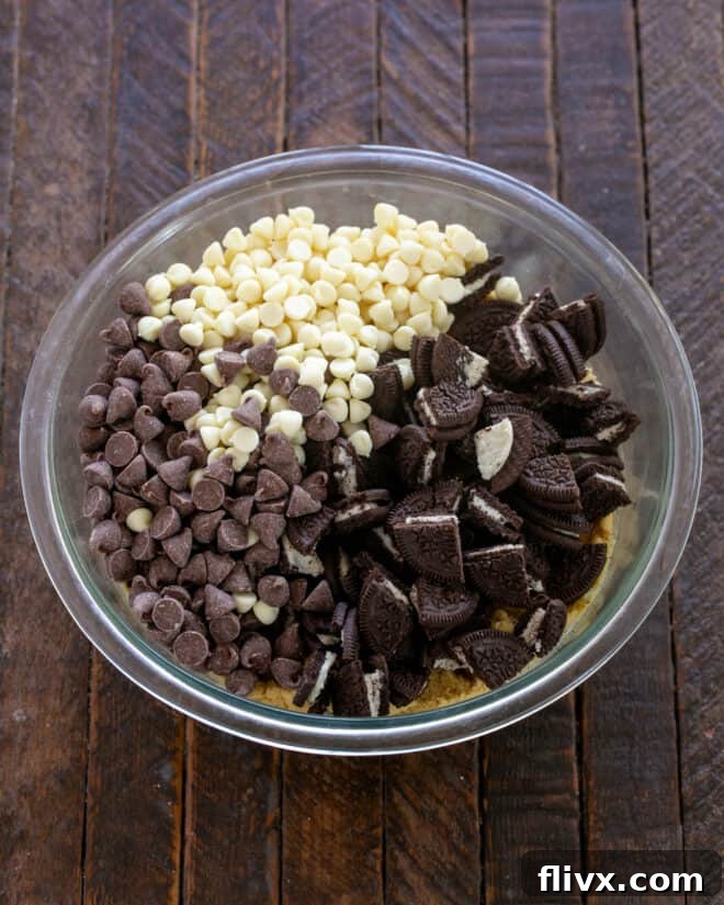 A spatula folding chocolate chips and chopped Oreo cookies into cookie dough.