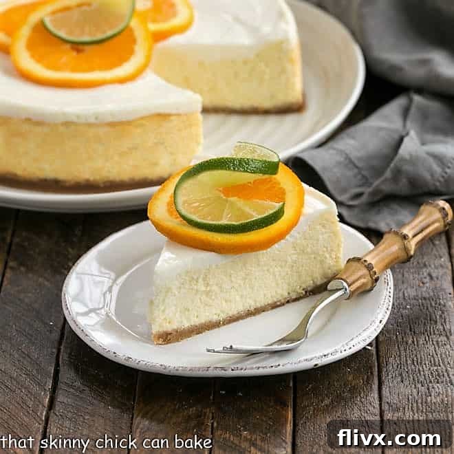 Margarita Cheesecake - An exquisite citrus cheesecake with the flavors of a margarita! A stunning close-up of a Margarita Cheesecake slice on a white plate, adorned with a delicate orange and lime slice. In the background, the full cheesecake with a slice removed reveals its creamy texture and golden crust.