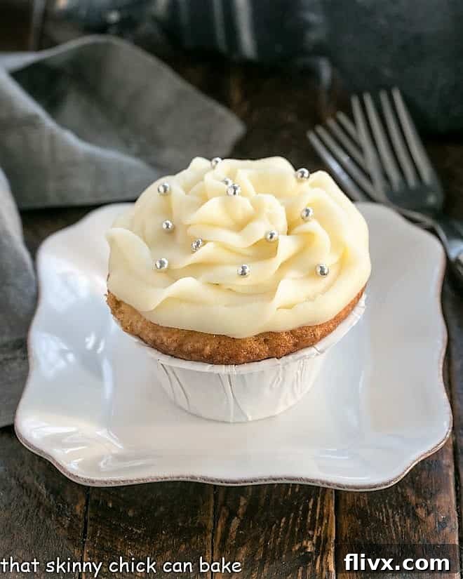 A single perfect vanilla cupcake with fluffy cream cheese frosting, presented on a minimalist square white plate.