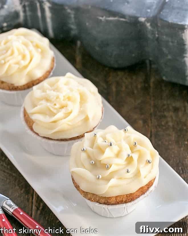 A trio of perfectly frosted Vanilla Cupcakes with Cream Cheese Frosting, presented on a sleek white rectangular tray, inviting indulgence.