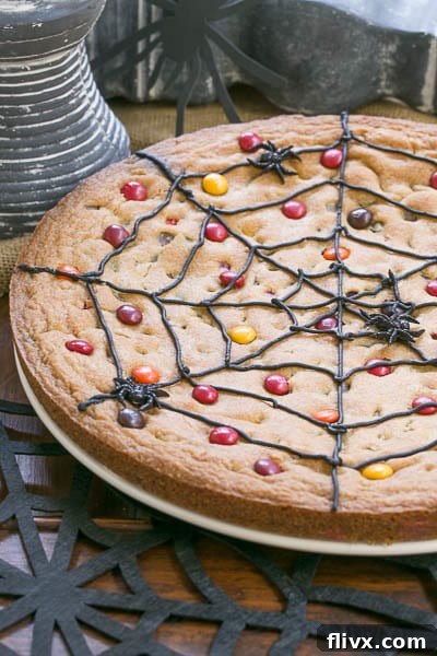 Close-up of a delightful Spiderweb Cookie Cake on a white plate, subtly enhanced by a black felt spiderweb underneath.