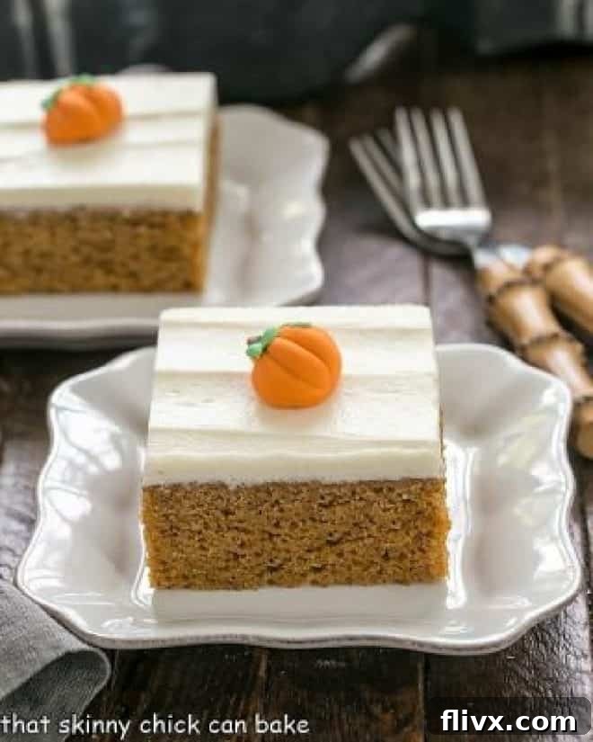Two pumpkin bars with a thick layer of cream cheese frosting and small candy pumpkins, served on elegant white dessert plates.