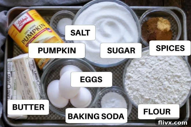 Various ingredients for pumpkin bars, including flour, sugar, pumpkin puree, eggs, and spices, neatly arranged on a metal tray with labels.