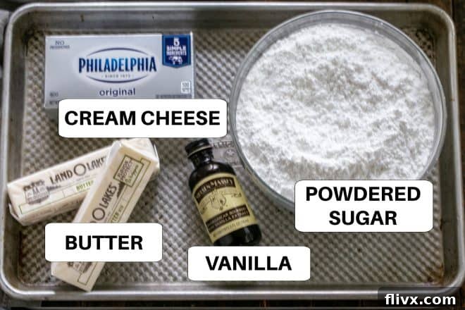 Ingredients for cream cheese frosting, including cream cheese, butter, vanilla extract, and powdered sugar, neatly arranged on a metal tray with labels.
