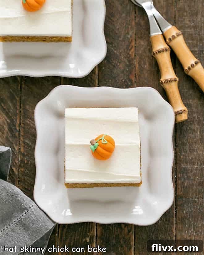 Overhead view of 2 Killer Pumpkin Bars with Cream Cheese Frosting on square white plates, garnished with small candy pumpkins.