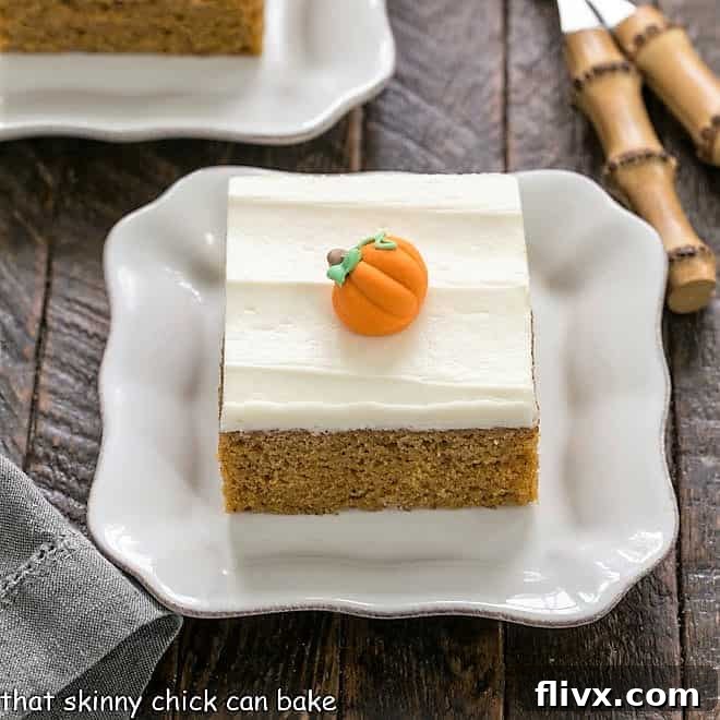 A single pumpkin bar with cream cheese frosting, served on a square white plate with two small bamboo forks, ready to be enjoyed.