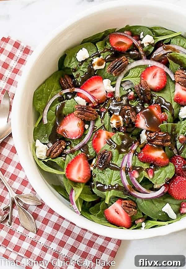 Close-up view of the vibrant Spinach, Strawberry, Pomegranate, Feta Salad, generously drizzled with a homemade balsamic vinaigrette, presented in a pristine white ceramic serving bowl.