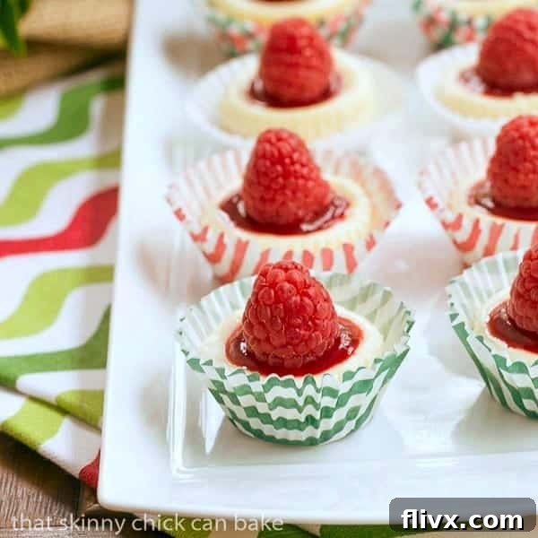 Mini Mascarpone Cheesecakes in red and green cupcake papers on a white tray, garnished with fresh raspberries.