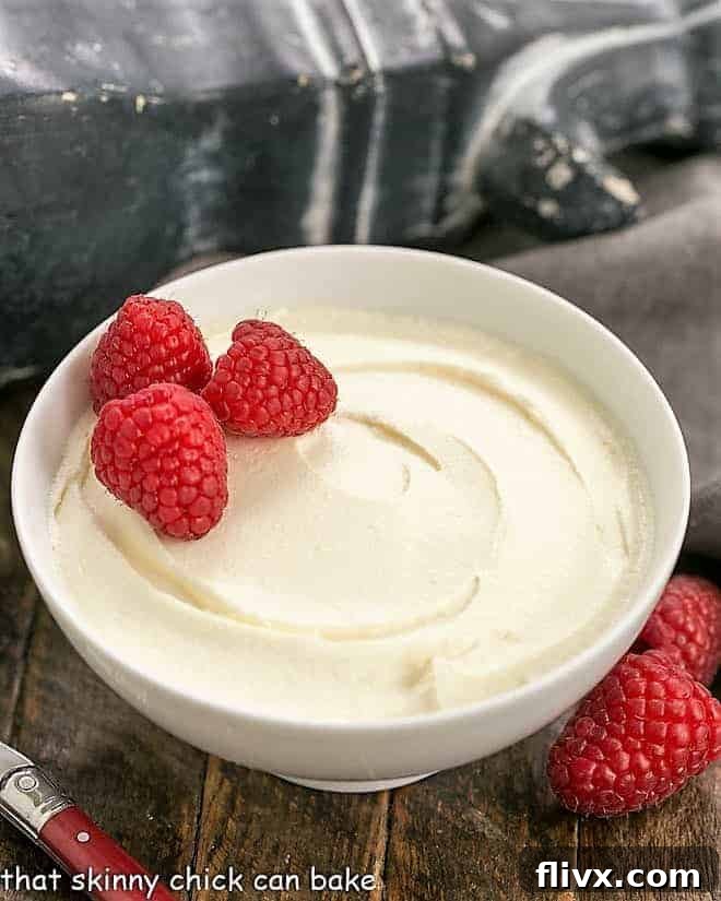 Homemade mascarpone cream in a white bowl garnished with fresh raspberries, showcasing its rich and smooth texture.