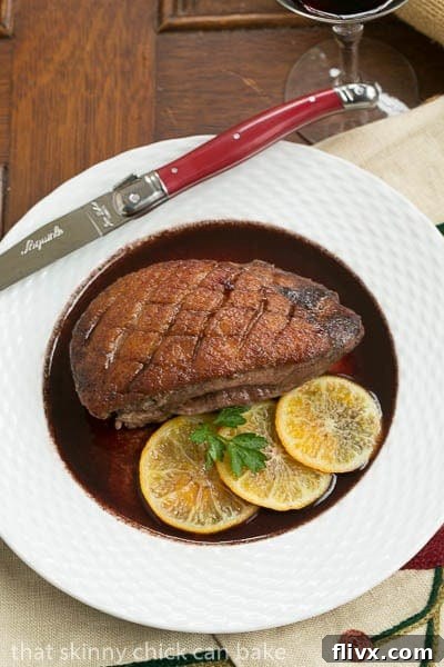 Pan Seared Duck Breasts in wine sauce on a white plate with a red handled knife and fork.