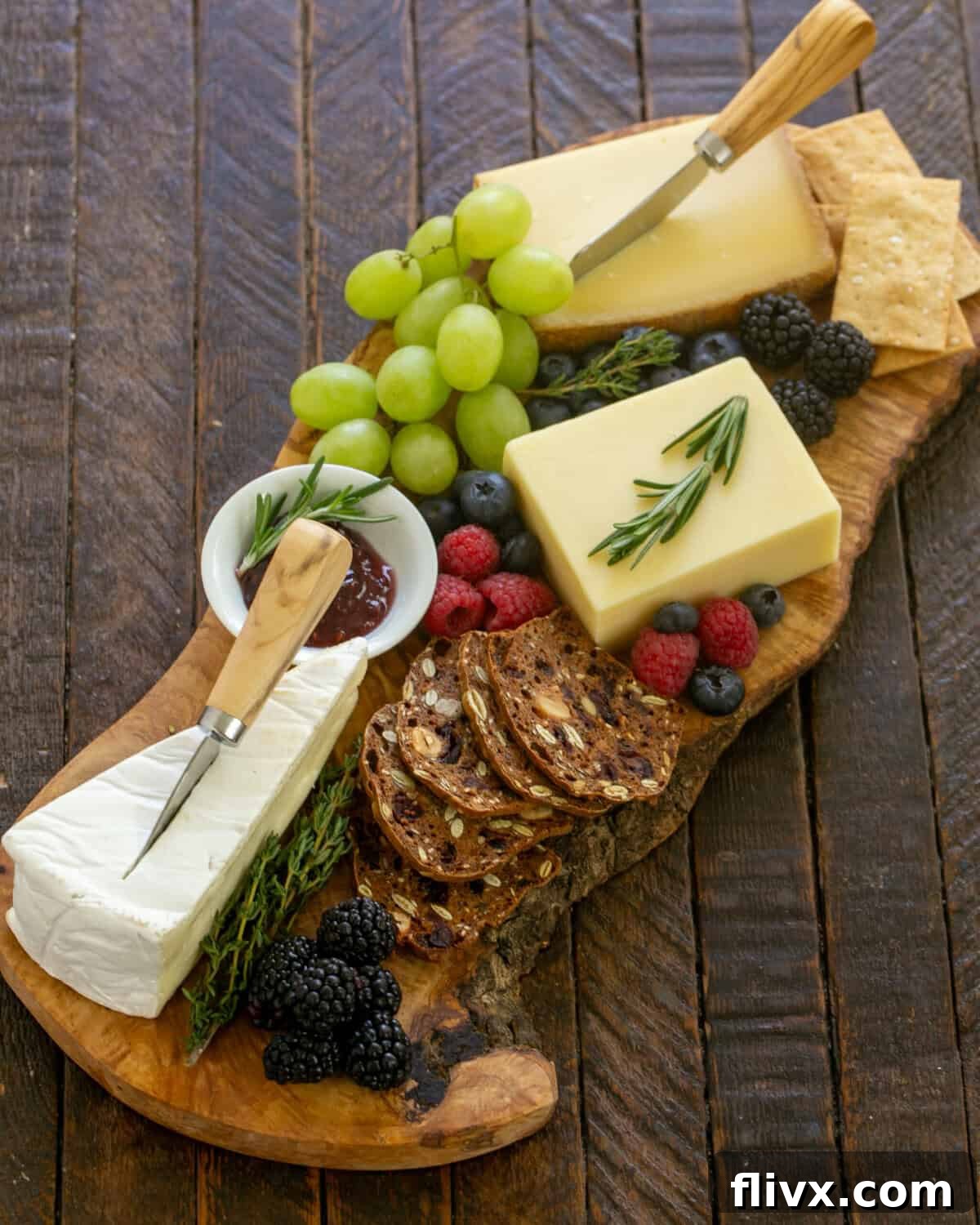 overhead view of wooden cheeseboard topped with fruit, cheese, and crackers.