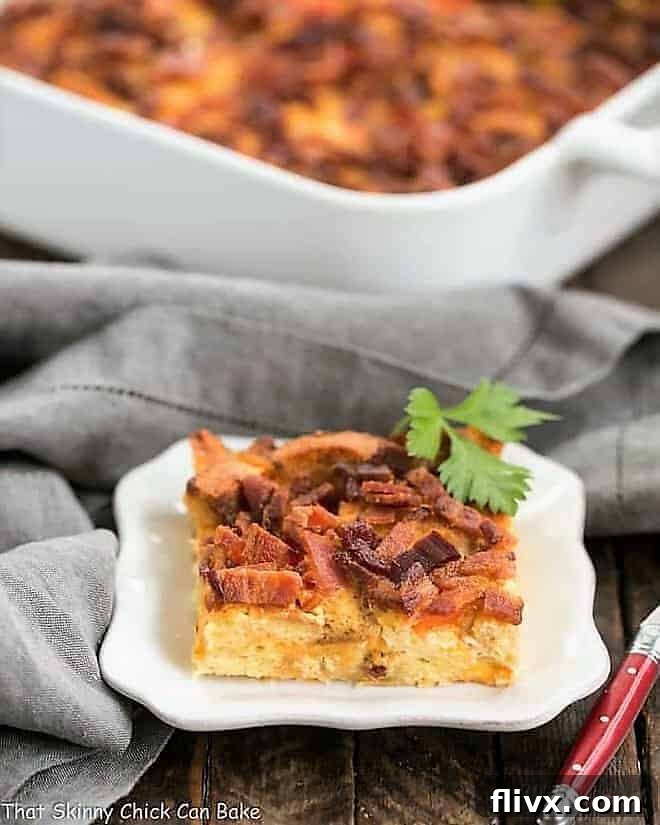 A perfectly portioned slice of Easy Bacon and Egg Strata on a pristine white plate, with the full casserole dish softly blurred in the background, showcasing its golden crust and savory layers.