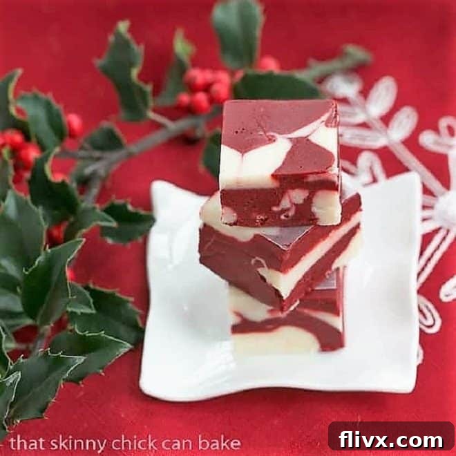 Stack of red velvet fudge on a small white plate with holly berries, emphasizing its festive appeal.