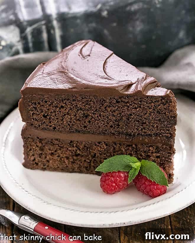 A beautiful slice of Devil's Food Cake on a white plate, adorned with fresh berries and a hint of mint, ready to be enjoyed. The deep chocolate color and rich frosting are enticing.