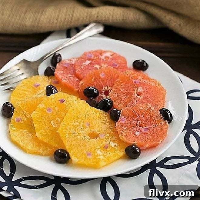 A selection of fresh ingredients for Moroccan Orange Salad, including vibrant oranges, dark Nicoise olives, and red onion slices, neatly arranged on a white plate, ready for preparation.