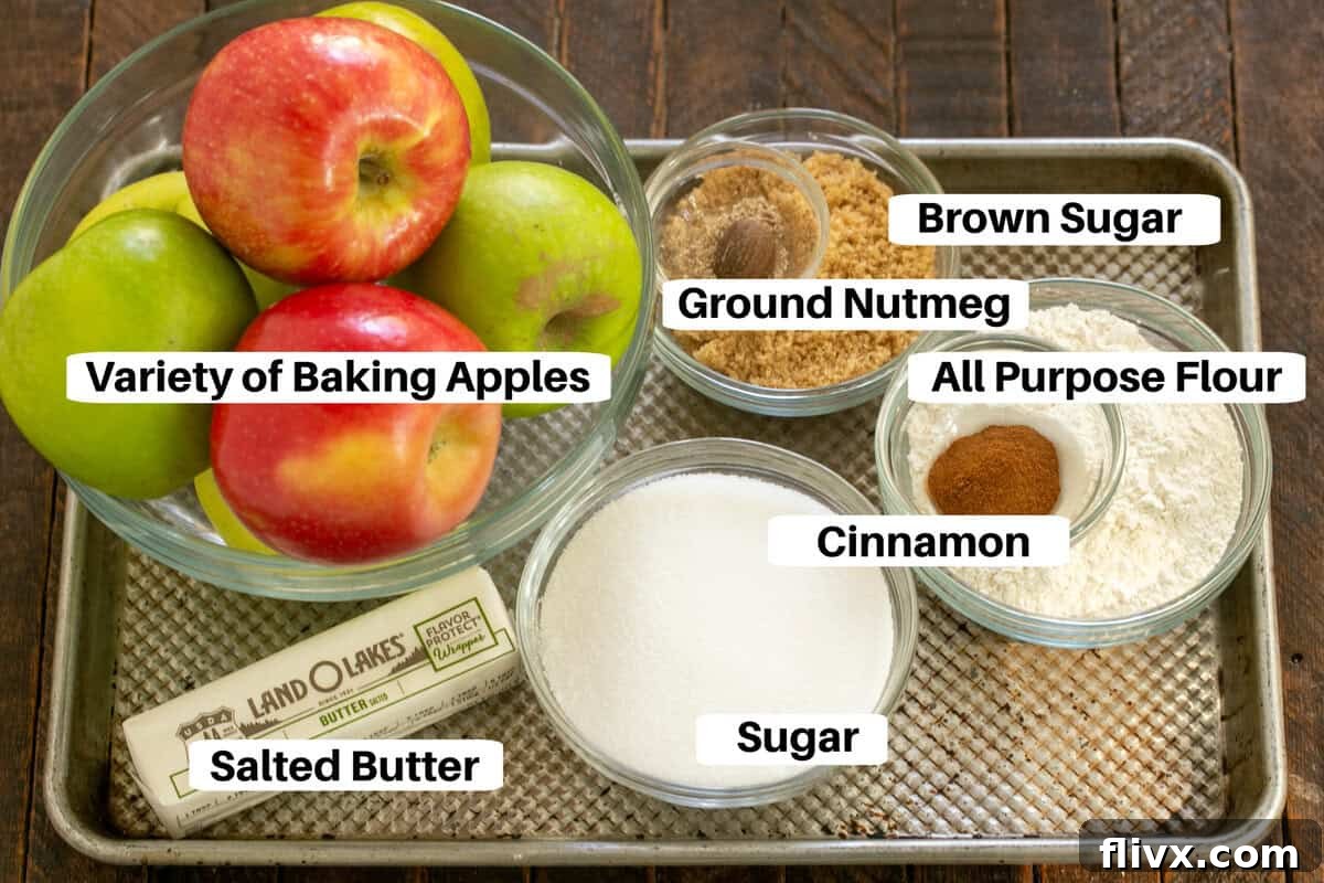 Apple crisp ingredients with labels on a metal sheetpan, showing fresh apples, flour, sugars, and spices.