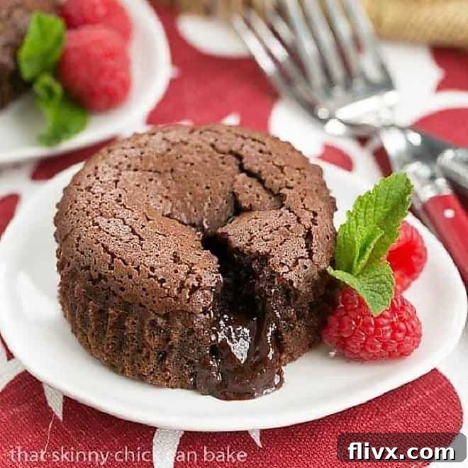 Chocolate Lava Cakes broken open on a white plate with raspberries and mint