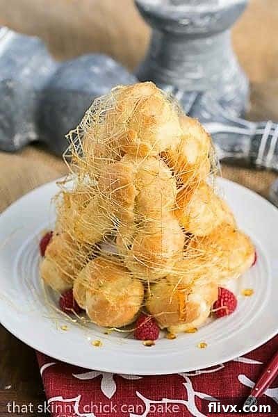 A close-up shot of the magnificent Lemon Cream Croquembouche, beautifully adorned with delicate spun sugar and fresh raspberries, displayed on a pristine white serving plate.