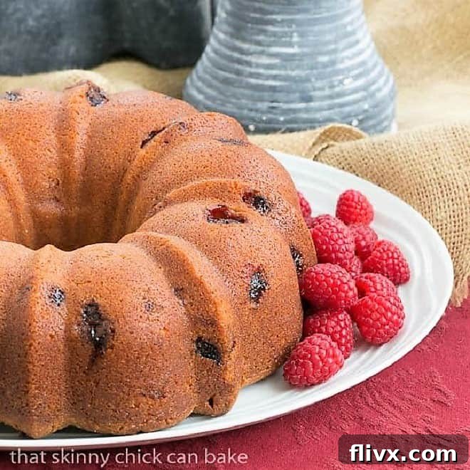 A beautifully glazed Raspberry Amaretto Bundt Cake on a cake plate, garnished with fresh raspberries and mint leaves, ready to be served.