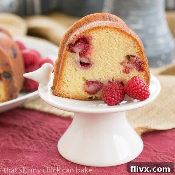 A single slice of Raspberry Amaretto Bundt Cake presented elegantly on a small white pedestal, showing its dense crumb and vibrant raspberries.