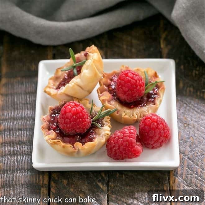 Raspberry Brie Bites on a white square plate, garnished with fresh raspberries and rosemary
