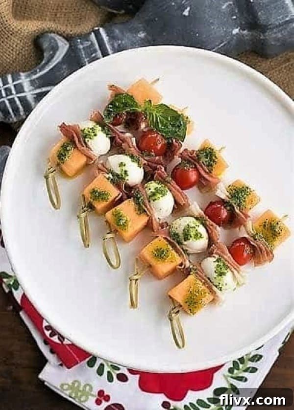 A collection of vibrant Melon and Prosciutto Skewers artfully arranged on a white cake stand, garnished with basil, ready for a summer party.