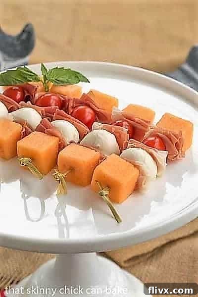 Close-up of Melon and Prosciutto Skewers artfully arranged on a white ceramic cake stand, highlighting the rich colors and textures of the ingredients.