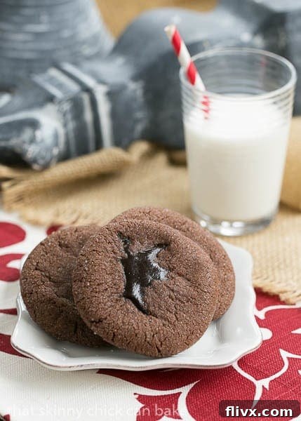 Three chocolate lava cookies on a small white plate with a tall glass of milk in the blurred background.