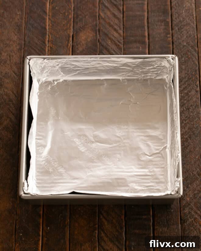 A baking pan being lined with non-stick foil, ready for brownie batter.