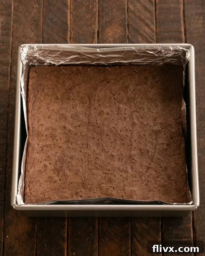 Brownie batter being spread evenly into the prepared baking pan.