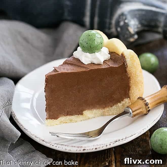 A slice of Irish Chocolate Mousse Cake on a white ceramic plate, garnished with whipped cream and a green candy.