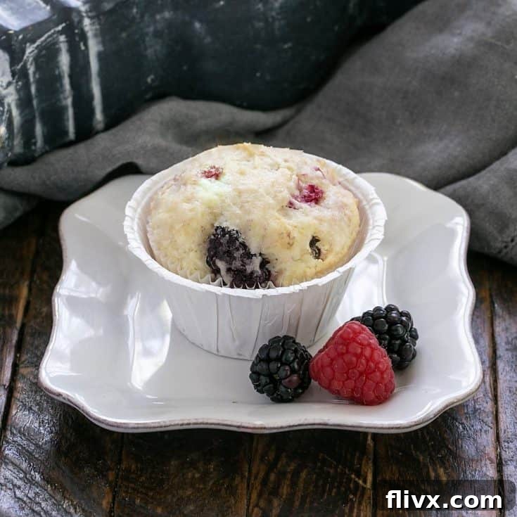 One berry muffin on a small white plate with a berry garnish