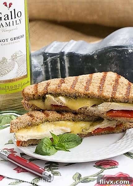 A perfectly golden-brown Chicken Pesto Grilled Cheese sandwich served on a white plate, resting on a floral napkin, inviting a delightful meal.