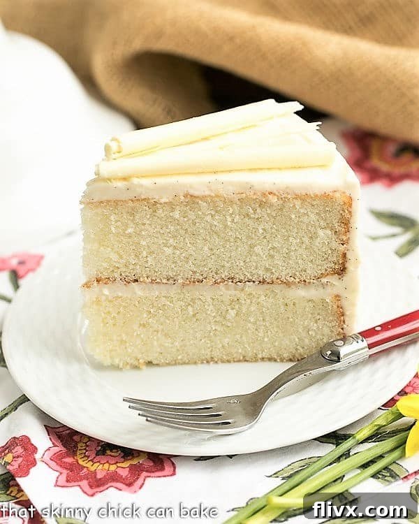 White birthday cake slice on a white plate over a floral napkin.
